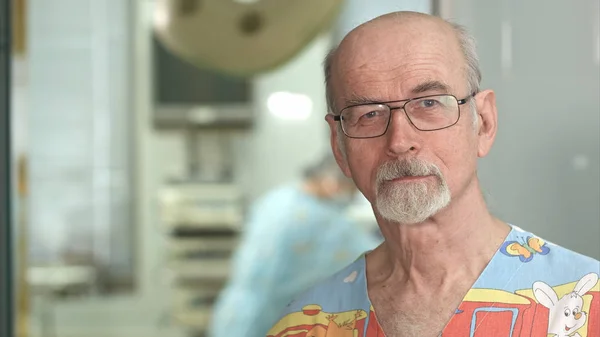 Senior mogen kirurg leende på kameran i sjukhuset kirurgi undersökning rum — Stockfoto