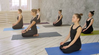 Grup pratik yoga, yoga mat üzerinde oturan genç kadını