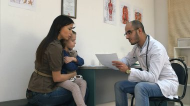 Genç doktor tıbbi sonuçları gösterilen genç anne küçük kız bardaklarda