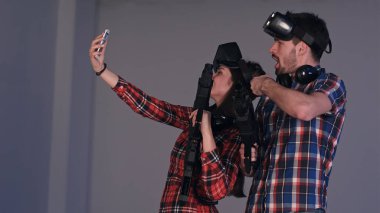 Genç adam ve sanal gerçeklik gözlükleri ve silah selfies telefonda alarak giyen kadın