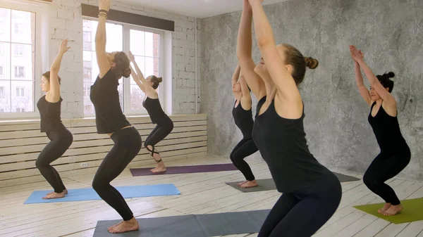 Women doing yoga sun salutation pose indoors at yoga studio