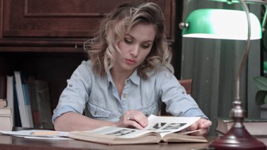 Düşünceli masasının üzerinde kitap okuyan genç kadın