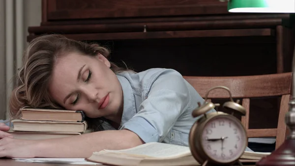 Mujer cansada tomando una siesta en un montón de libros y siendo despertada por una alarma — Foto de Stock