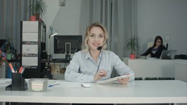 Tablet kullanma ve kameraya konuşurken gülümseyen Çağrı Merkezi müşteri temsilcisi