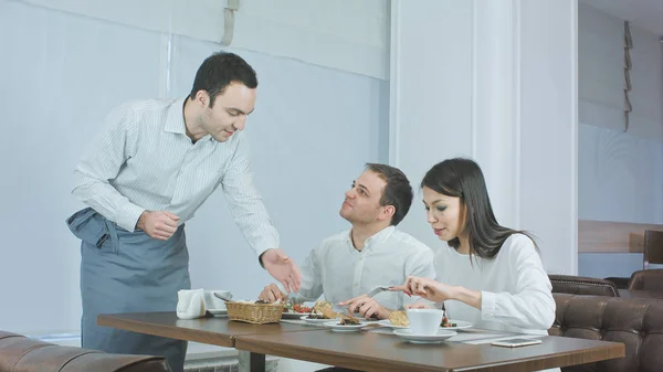 Pareja joven disfrutando de su almuerzo en el restaurante cuando el camarero trae más comida —  Fotos de Stock