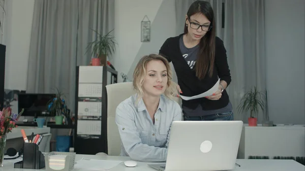 Two happy office women coworking on a report using the laptop