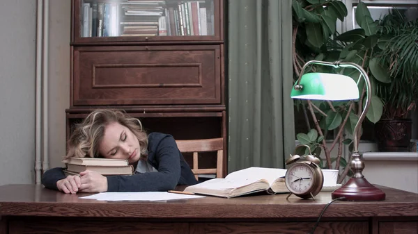 精疲力竭的女性睡着的书在她的书桌上的堆栈上，并很快被闹钟吵醒了需要她的书和报纸、 喝咖啡和叶 — 图库照片