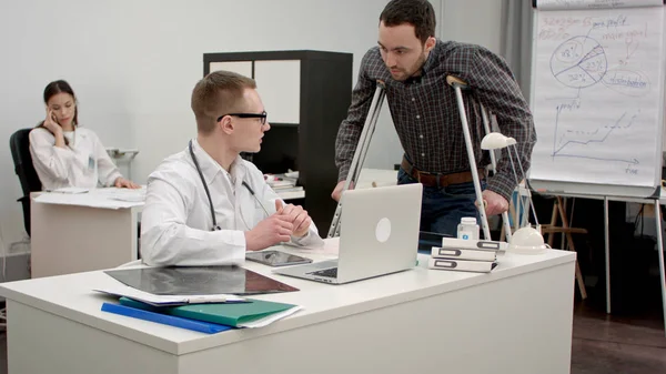 Чоловік лікар обговорює рентген хребта з пацієнтом на милицях — стокове фото