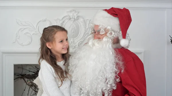 Χαριτωμένο μικρό κορίτσι ένα τραγούδι Χριστουγέννων κάθεται στην αγκαλιά του Άγιου Βασίλη — Φωτογραφία Αρχείου