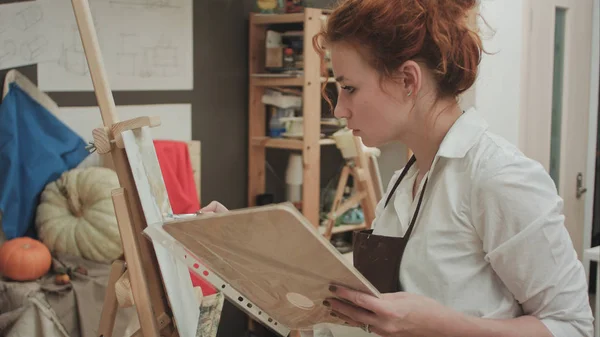Giovane donna in grembiule pittura con olio su tela bianca — Foto Stock