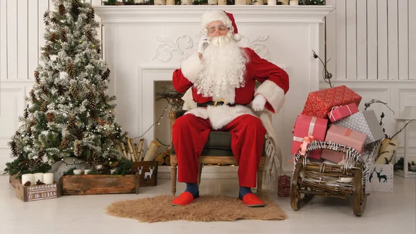 Papai Noel alegre sentado junto à árvore de Natal e falando ao telefone — Fotografia de Stock