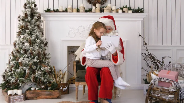 Menina sentada com Papai Noel grave usando tablet — Fotografia de Stock