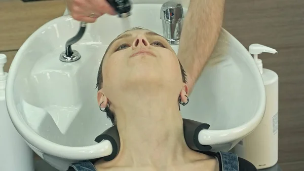 Beautiful young girl enjoying hair washing in hairdressing salon.