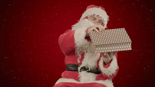 Weihnachtsmann mit einem Geschenk in der Hand auf rotem Hintergrund mit Schnee — Stockfoto