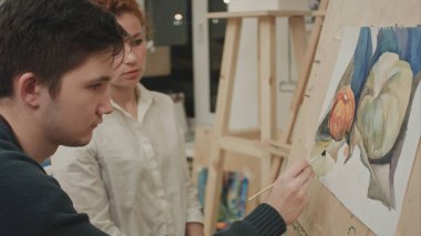 Kadın sanatçı suluboya ile boyamak için genç erkek öğrenci öğretim