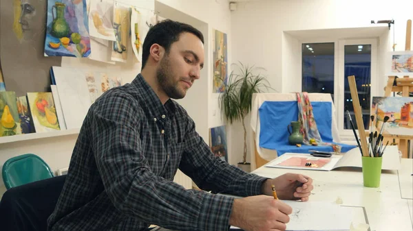 Estudante de arte do sexo masculino fazendo um esboço com um lápis sentado na mesa em estúdio — Fotografia de Stock