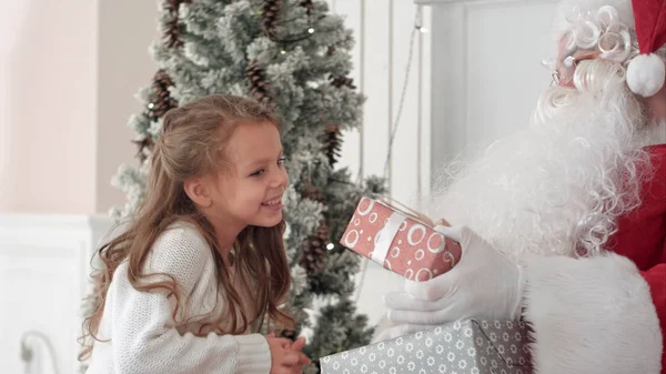 Santa Claus αγκαλιάζει ένα μικρό χαριτωμένο κοριτσάκι, και δίνοντας τα Χριστούγεννα παρουσιάζουν — Φωτογραφία Αρχείου