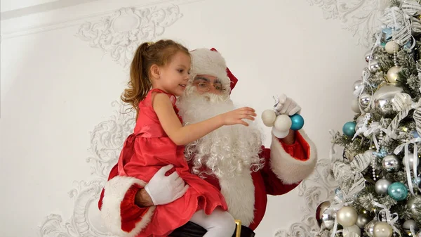 Santa Claus βοηθώντας κοριτσάκι να κρεμάσετε τα στολίδια επάνω από το χριστουγεννιάτικο δέντρο — Φωτογραφία Αρχείου