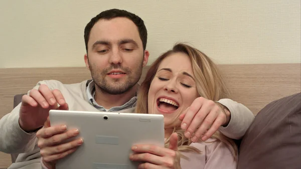 Молода пара в ліжку використовує цифровий планшет, посміхається і сміється — стокове фото