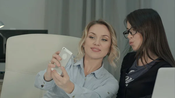 Дві жінки-колеги беруть селфі з телефоном, сидячи за столом — стокове фото
