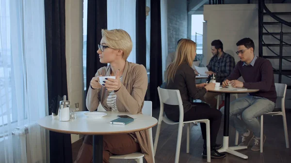 Jovem bela mulher sentada à mesa e bebendo café interior — Fotografia de Stock