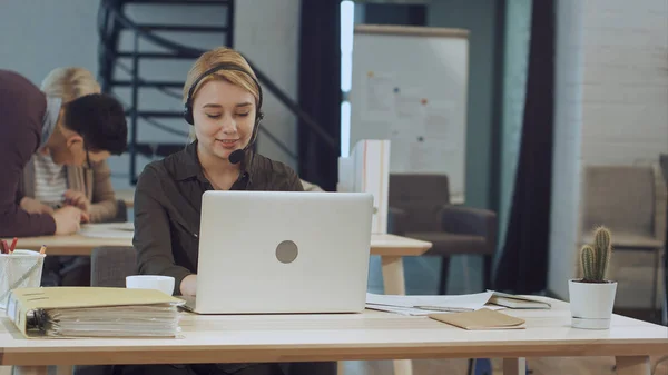 漂亮的女商人头戴耳机和手提电脑在办公桌前工作的画像 — 图库照片