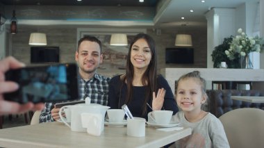 Birisi cep telefonu kafede genç mutlu aile fotoğrafı çekmek.