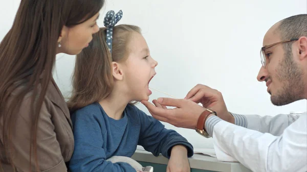 Niña que se somete a examen de garganta con depresor de la lengua por un médico masculino — Foto de Stock