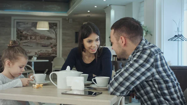 Семья наслаждается чаем в кафе вместе. Отец и мать разговаривают, глядя на свою дочь . — стоковое фото