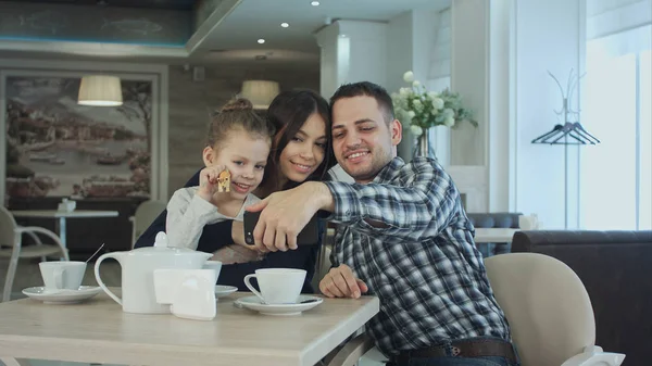 Beautiful young family taking selfie on smartfone while enjoying their time in cafe.