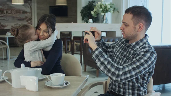 Father taking lovely photos of mother and daughter kissing and hugging.