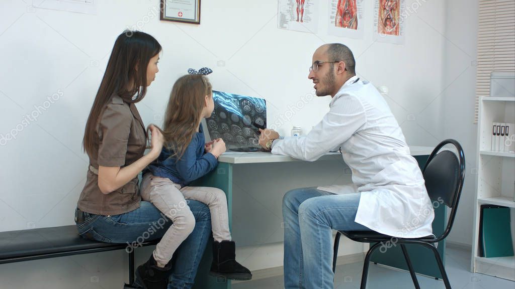 Doctor showing xray image to young mother with cheerful daughter