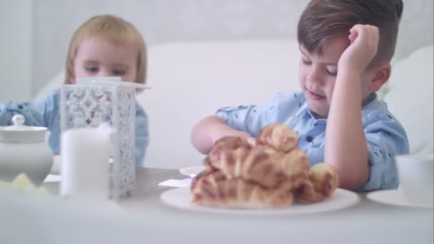 Два милых маленьких мальчика веселятся за чайным столом с выпечкой — стоковое видео