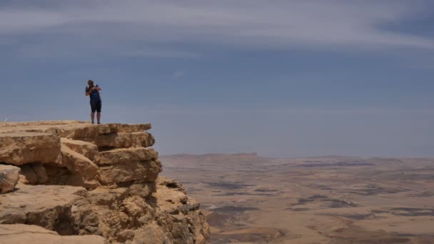 Junger Mann steht auf Klippe und macht mit seinem Handy Fotos von der Wüste — Stockvideo