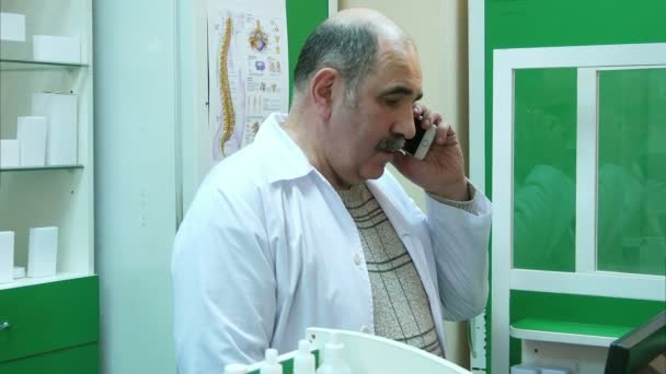 Senior farmaceuty rozmowy na telefon komórkowy podczas sprawdzania recepty w aptece — Wideo stockowe