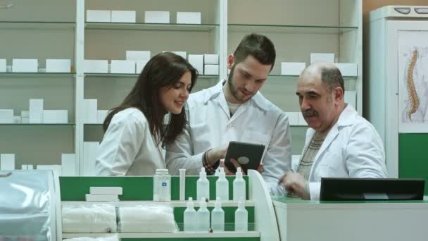 Lächelndes Apothekerteam, zwei Männer und eine Frau, stehen nebeneinander in der Apotheke und prüfen Informationen auf einem Tablet-Computer — Stockvideo