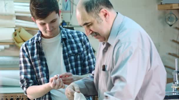 Operaio anziano che posa una benda sulla ferita al dito del giovane tirocinante in laboratorio telaio — Video Stock