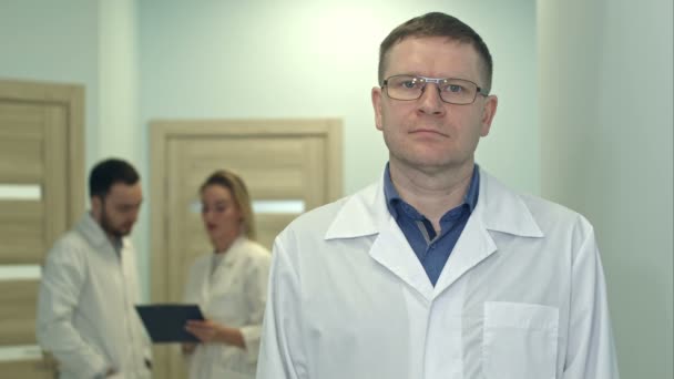 Male doctor looking at camera while medical staff working on the background — Stock Video