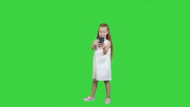 Glückliches kleines Mädchen macht ein Selfie mit einem Smartphone auf einem grünen Bildschirm, Chroma-Schlüssel — Stockvideo