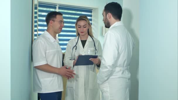 Двоє чоловіків-лікарів обговорюють питання, коли медсестра робить нотатки — стокове відео