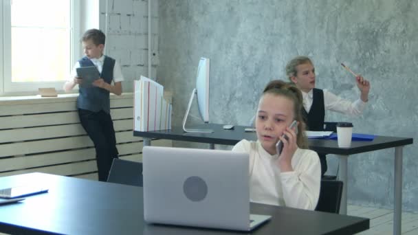 Retrato de una niña hablando por teléfono y trabajando en el ordenador portátil en la oficina — Vídeo de stock