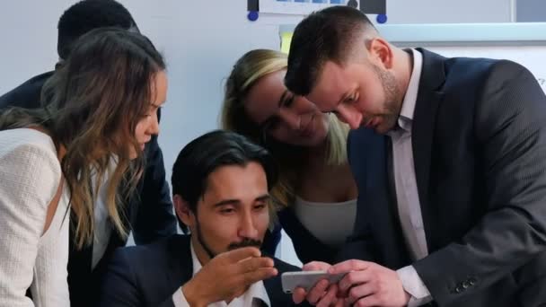 Усміхнена ділова команда, що працює зі смартфоном, дивиться дещо цікаве в офісі — стокове відео