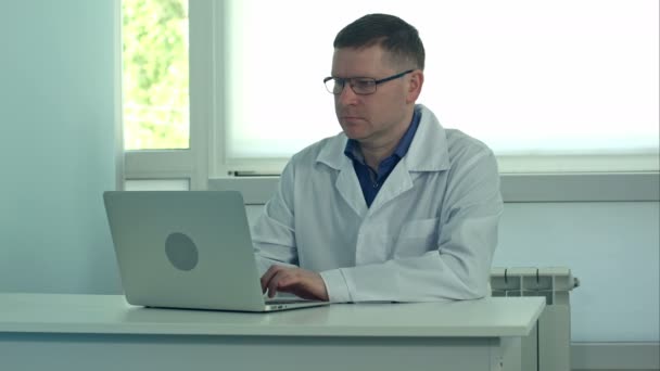 Médico masculino trabajando en computadora portátil en escritorio blanco en el hospital — Vídeo de stock