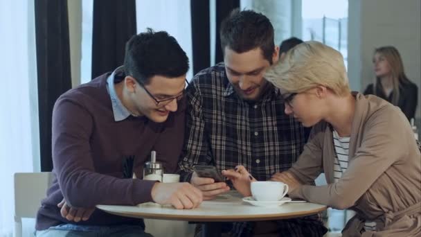 Gruppen av unga kreativa människor bär business casual kläder samarbetar vid mötesbord och diskutera arbetet, med hjälp av smartphone — Stockvideo