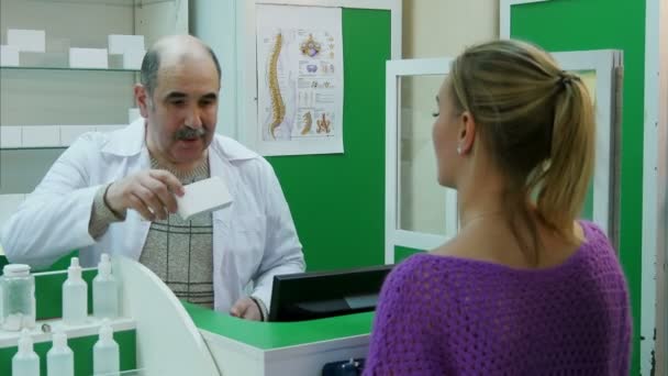 Ανώτερος φαρμακοποιός βοηθώντας ένα θηλυκό πελάτη στο κεφάλι του μια ουρά στο φαρμακείο — Αρχείο Βίντεο
