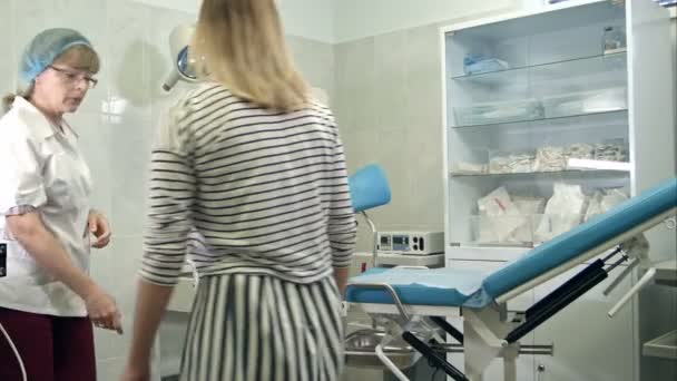 婦人科医は、女性の患者に検査のために婦人科の椅子に座るように頼む — ストック動画