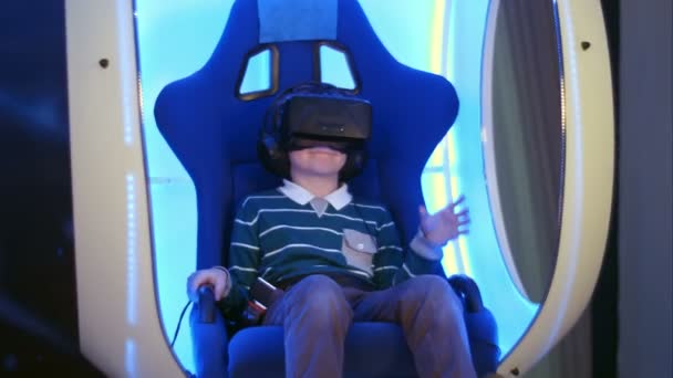 Niño sorprendido experimentando la realidad virtual en una silla interactiva en movimiento — Vídeo de stock