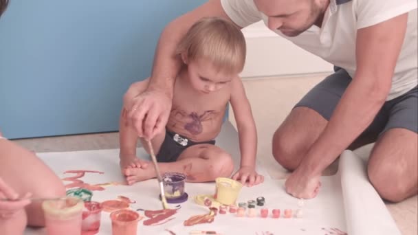 Jonge vader die zijn kind jongen onderwijzen hoe te schilderen — Stockvideo