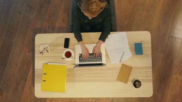 Mooie jonge vrouw zit aan het bureau en typt op laptop — Stockvideo