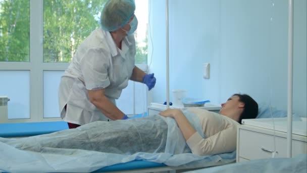 Krankenschwester in Handschuhen und Maske legt Patientin auf Krankenhausstation am Tropf — Stockvideo